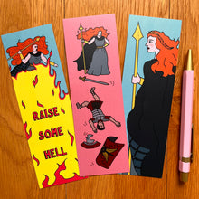 Load image into Gallery viewer, Three bookmarks laid out each with a different image celebrating Boudicca. One shows her wielding a spear with a crown in her ginger hair; another raising it above a blaze of fire captioned “raise some hell”; another having dispatched a Roman soldier who is tumbling down the bookmark with his weapon and armour falling around him. Pictured here with a pink pen to match the pink background of some of the bookmarks.