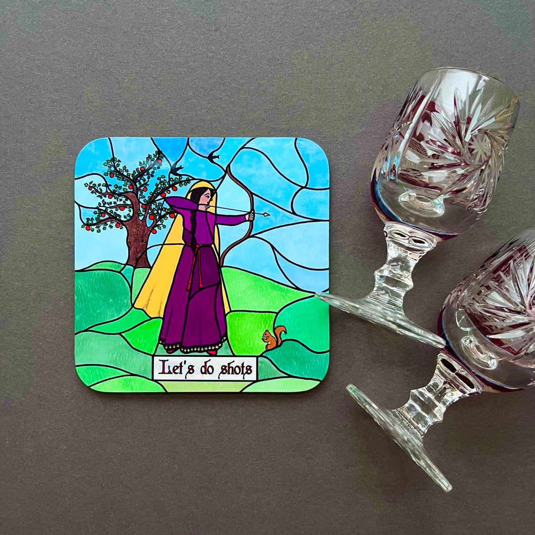 Photo of a coaster with artwork in stained glass style of a woman in a purple dress holding a bow with the arrow drawn in front of a tree, with a squirrel at her feet. The caption reads “Let’s Do Shots”. Next to the coaster is two glasses.