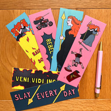 Load image into Gallery viewer, One bookmark shows her wielding a spear with a crown in her ginger hair; another raising it above a blaze of fire captioned “raise some hell”; another having dispatched a Roman soldier who is tumbling down the bookmark with his weapon and armour falling around him; a fourth has her riding a motorbike with her cape flapping in the wind, above the caption “rebel queen”; another with the caption “slay every day” in between spears; and the last with the caption “veni.vidi.incanvidi” surrounded by fire.