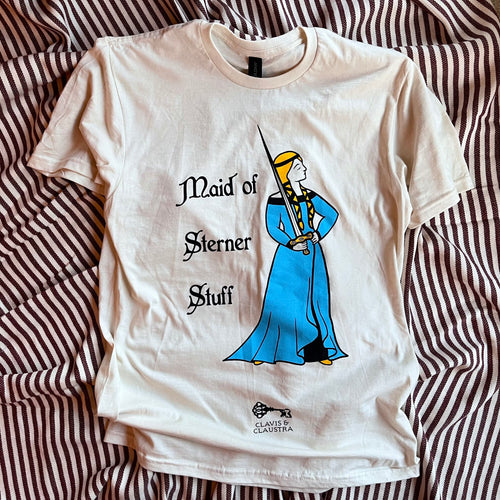 Photo of natural cotton / cream t-shirt laid out on cream and burgundy striped fabric. Featuring an illustration in black, sunflower yellow and sky blue of a damsel in medieval dress with plaited hair casually holding a sword, beside the text 